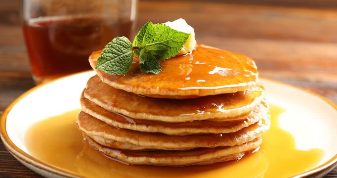 Man adding mint to pancakes with maple syrup at table, closeup