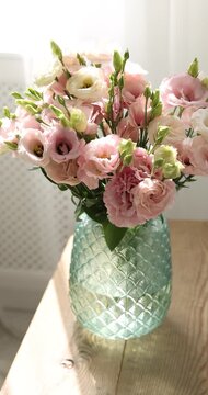 Bouquet of beautiful eustoma flowers in vase on wooden bench indoors, closeup. Camera moving forward