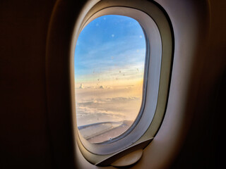 Naklejka premium View of soft clouds and blue sky during sunset from an airplane window frame, ideal for travel concept.