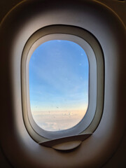 Fototapeta premium View of soft clouds and blue sky during sunset from an airplane window frame, ideal for travel concept.