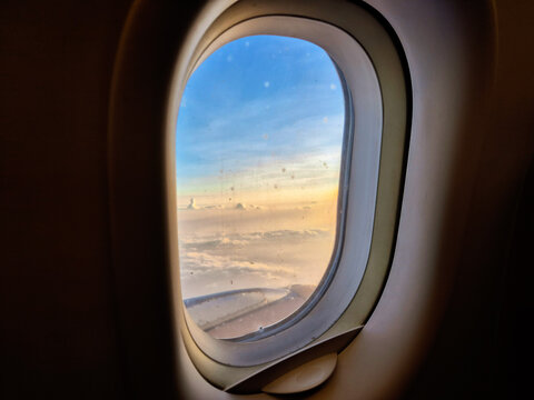 View of soft clouds and blue sky during sunset from an airplane window frame, ideal for travel concept.