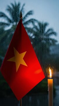 Vietnamese flag and burning candle by a rainy window representing mourning remembrance and patriotism
