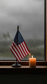 American flag and a burning candle on a wooden windowsill on a rainy day representing remembrance, patriotism, and solemn reflection