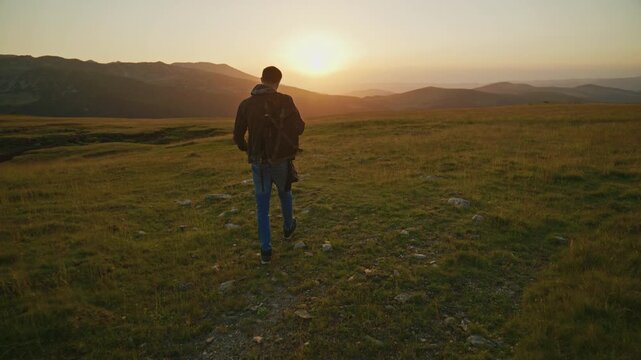 Sunset walk on a mountain trail with a person heading towards a distant horizon and trees in the background