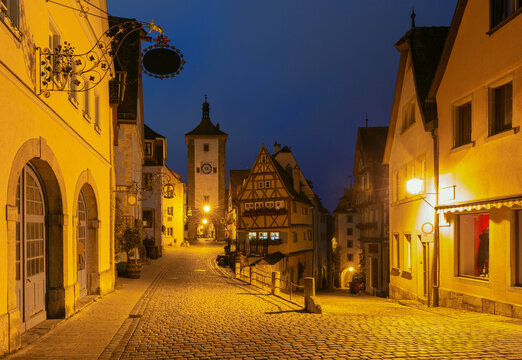 Half-timbered houses and cobblestone streets illuminated by warm streetlights during blue hour in Rothenburg ob der Tauber, Germany.