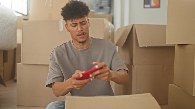 Man holding red smartphone and gesturing with hand among cardboard moving boxes in a building; distraction packing day.