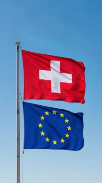 Swiss and European Union flags waving together on a flagpole against clear blue sky representing international relations