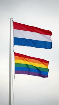 Netherlands flag and rainbow pride flag waving together on a flagpole representing diversity and equality in Dutch society