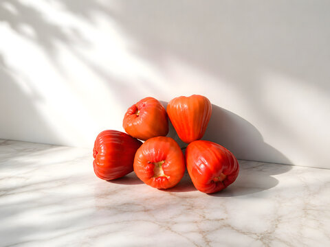 Fresh Red Wax Apples Arranged on a White Marble Surface with Soft Natural Sunlight and Shadows