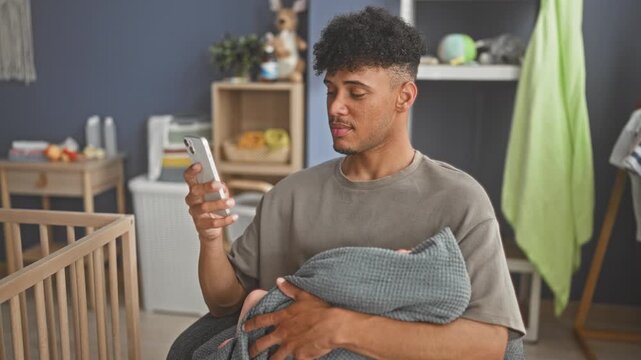 Man cradling baby in a grey blanket, hand holding smartphone and resting on cradle rail in nursery building; parental tenderness.