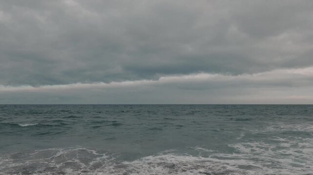 Intermittent waves breaking on a gray sandy beach beneath a gray sky
