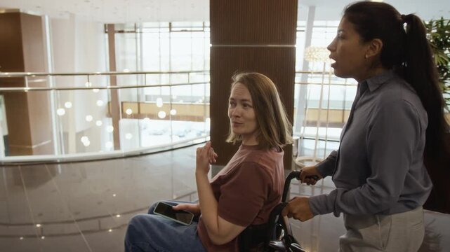 Caucasian woman with disability in wheelchair being pushed by Hispanic young adult assistant. Clip is ideal for healthcare and diversity marketing campaigns