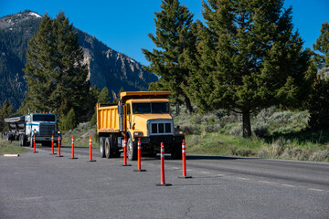 Summer construction season, bright yellow dump truck on road with side dumper truck behind, summer vacation at Yellowstone National Park  © knelson20