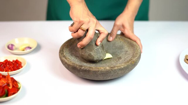 Female hands grinding fresh garlic and shallots in a traditional stone mortar and pestle