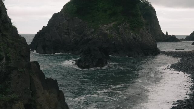 Waves crashing onto a beach beneath steep coastal cliffs