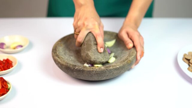 Female hands grinding fresh spices with traditional stone mortar and pestle on white table