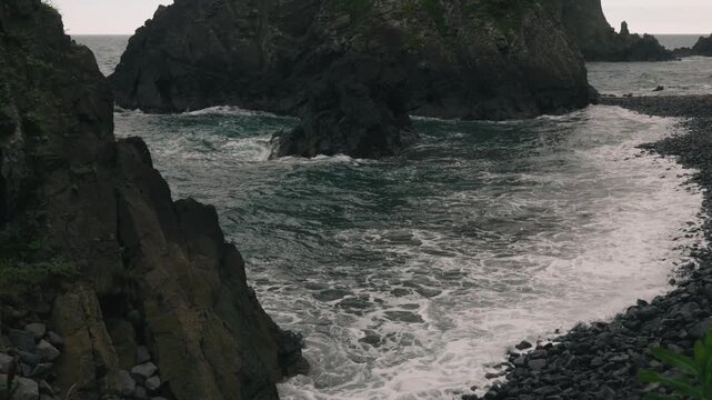 Waves crashing onto a beach beneath steep coastal cliffs
