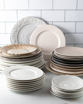 Stacks of assorted plates on a light surface against a subway tile background.