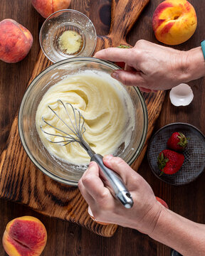 A hand vigorously stirring cake batter for making a strawberry peach cake.