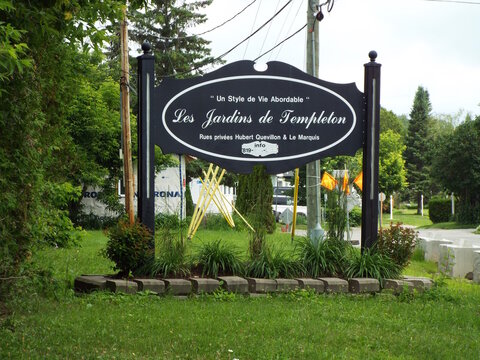 Gatineau, Quebec, Canada &ndash; June 28, 2026: A decorative black sign for "Les Jardins de Templeton" stands outdoors amidst lush green grass, trees, and landscaping foliage on Bd Saint-Ren&eacute; E.