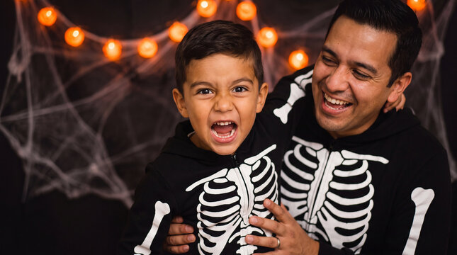 Father and son in matching skeleton costumes laughing with silly scary faces during Halloween celebration, great for spooky themed advertising and posters.
