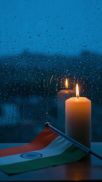 Indian flag and burning candle on a rainy window sill representing patriotism and mourning for editorial and conceptual use
