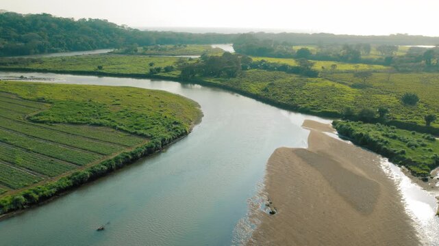 Aerial view of river merging with the ocean coast and green pastures in Costa Rica