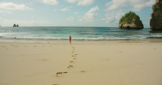 Woman in swimwear walks toward turquoise ocean waves on white sand beach at Diamond Beach