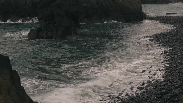 Waves crashing onto a beach beneath steep coastal cliffs