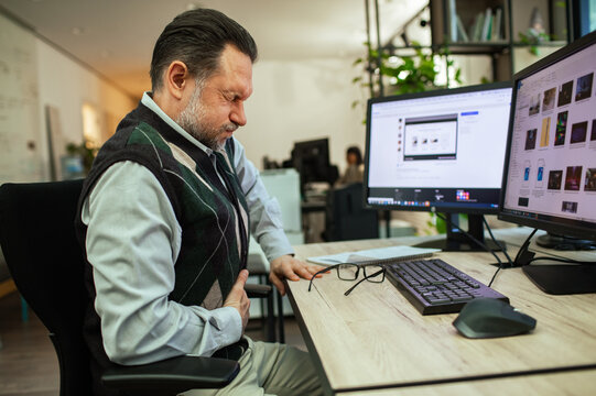Middle-aged office worker holding stomach in pain at desk