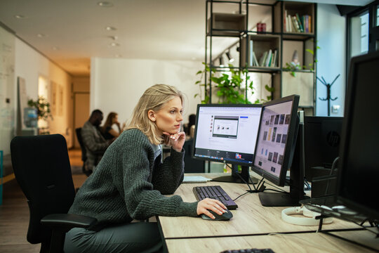Focused woman working at dual monitors in modern office