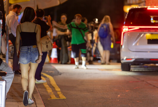 A sexy female figure,  walks along Lan Kwai Fong's bustling bar street at night.