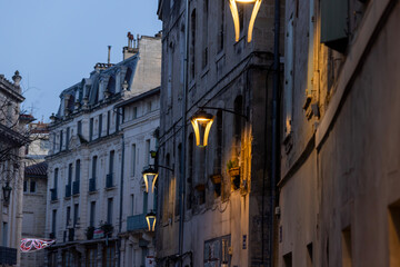 Fototapeta premium Night falls on ancient stone streets, where wall lamps cast light over historic architecture and rooftops.