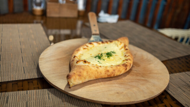 Khachapuri - A traditional boat-shaped cheese bread topped with fresh dill rests on a wooden plate.