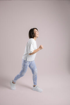 [Pink Background] A woman smiling as she enjoys running or walking; an active woman in her 40s who exercises to stay healthy