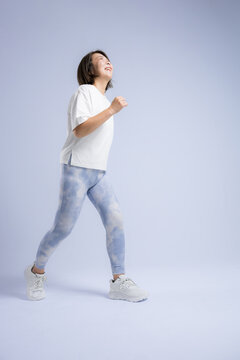 [Light blue background] A woman smiling as she enjoys running or walking; an active woman in her 40s who exercises to stay healthy