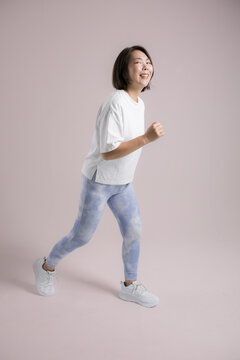 [Pink Background] A woman smiling as she enjoys running or walking; an active woman in her 40s who exercises to stay healthy