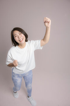 [ピンク背景]笑顔でガッツポーズで腕を高く伸ばして運動する女性、ダイエット成功や健康的で前向きな40代のミドル世代のフィットネスイメージ