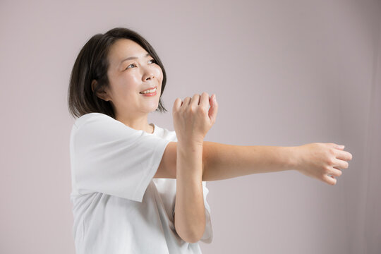 [ピンク背景]更年期も健康のために笑顔でストレッチする40代女性、運動前に体をほぐすのフィットネス