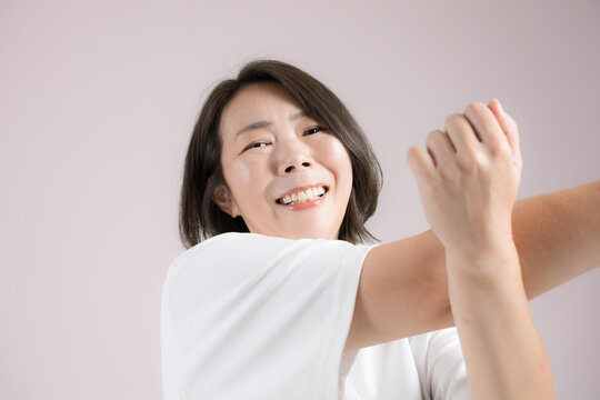 [ピンク背景]更年期も健康のために笑顔でストレッチする40代女性、運動前に体をほぐすのフィットネス