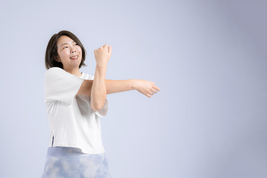 [ブルー背景]更年期も健康のために笑顔でストレッチする40代女性、運動前に体をほぐすのフィットネス
