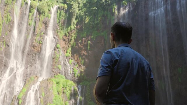 Young man admiring an impressive waterfall in a forest
