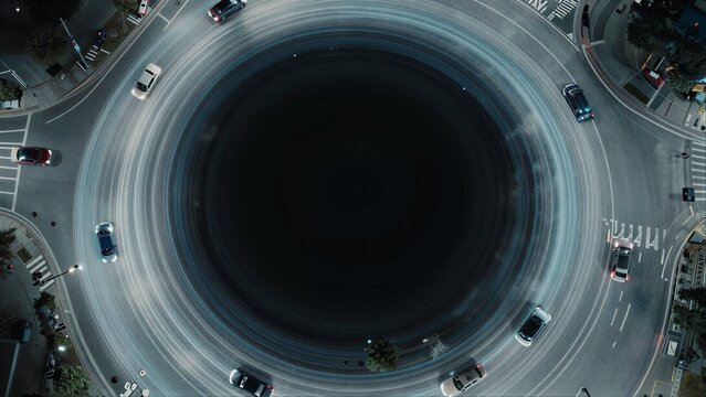 Cars swirl in a circular motion around a dark, hypnotic center at night.