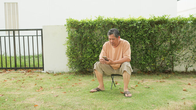 Senior Asian man sitting alone on folding stool in garden looking thoughtful