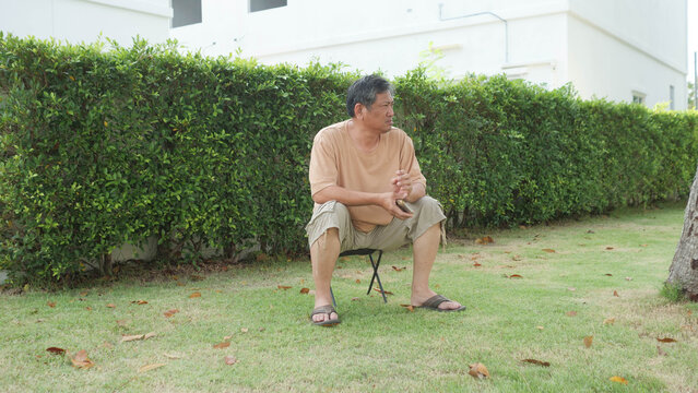Senior Asian man sitting alone on folding stool in garden looking thoughtful