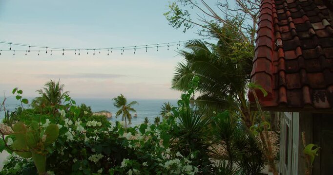 bungalow roof and string lights frame coastal view of palm trees in Nusa Penida Island Bali