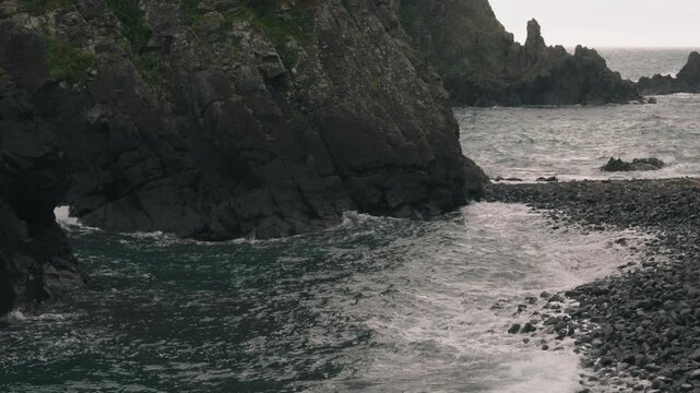 Waves crashing onto a beach beneath steep coastal cliffs