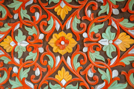 Traditional Minangkabau wood carving featuring intricate floral motifs, curling vines, and colorful symmetrical ornamental patterns inspired by Indonesian cultural heritage.