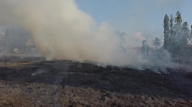 Grass on a soccer field burning in flames. The scene shows fire spreading across dry grass in an outdoor sports area, creating smoke and visible fire damage.