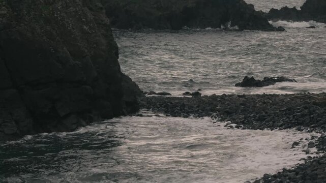 Waves crashing onto a beach beneath steep coastal cliffs